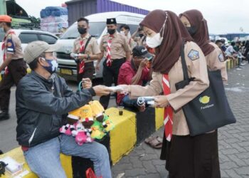 Scout volunteers distributing face masks to a children-toys seller in a bus terminal.