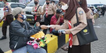 Scout volunteers distributing face masks to a children-toys seller in a bus terminal.