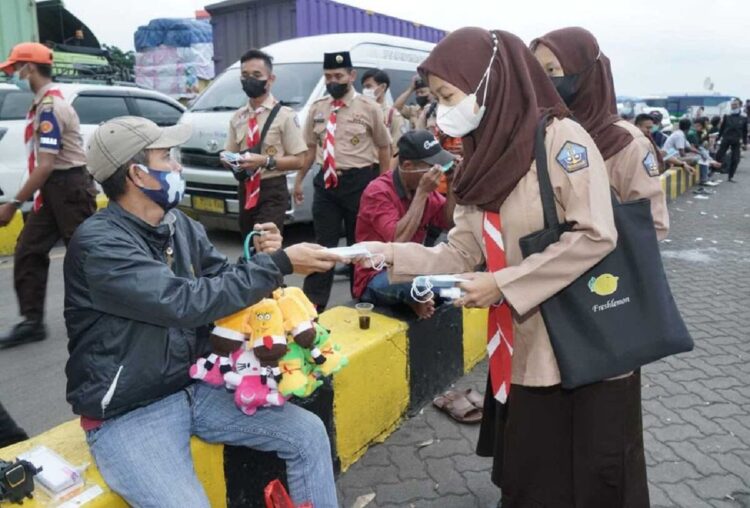 Scout volunteers distributing face masks to a children-toys seller in a bus terminal.